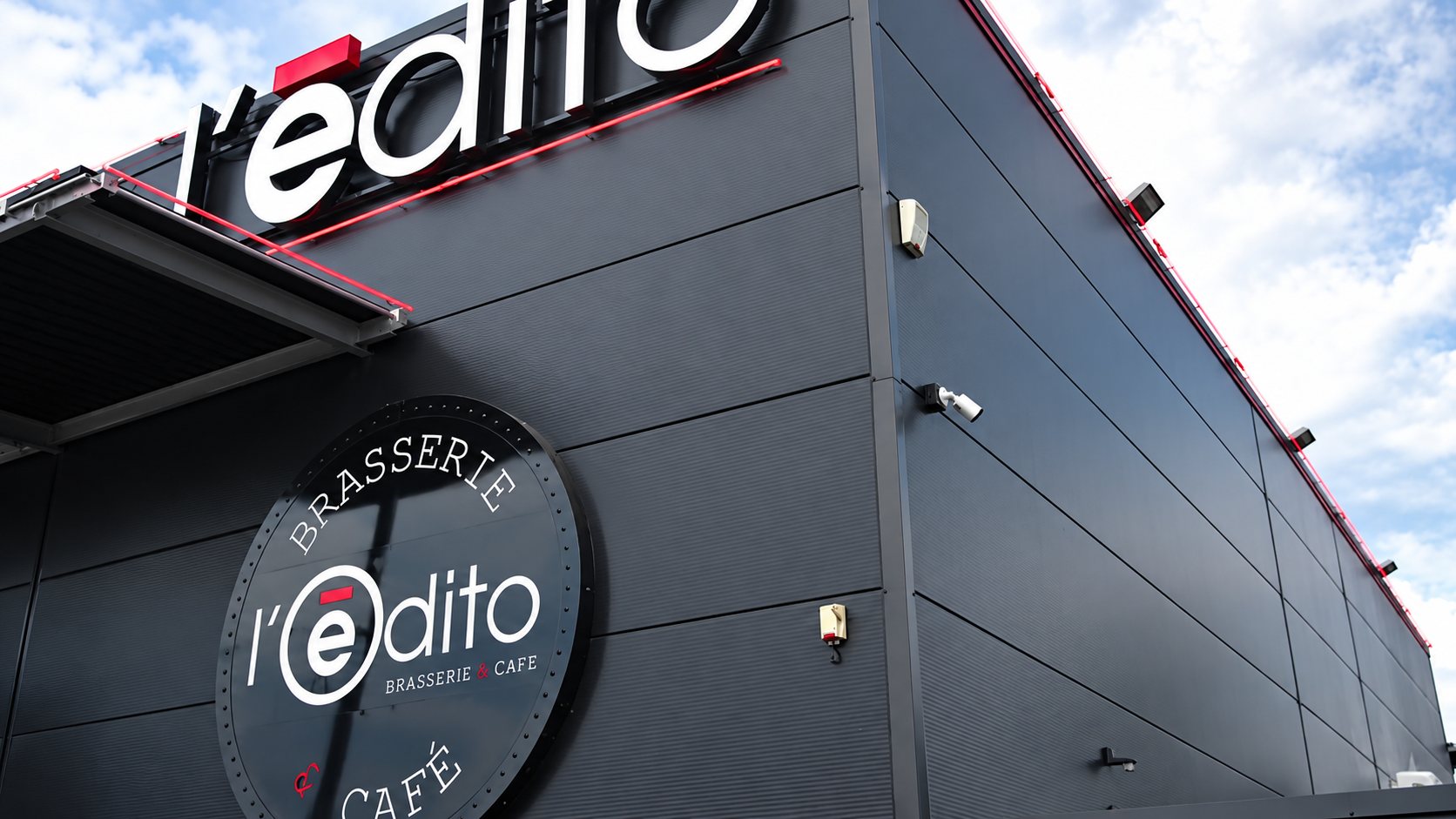 Façade en bardage noir de la brasserie café L'Edito, avec son enseigne lumineuse en lettres blanches et son logo circulaire.