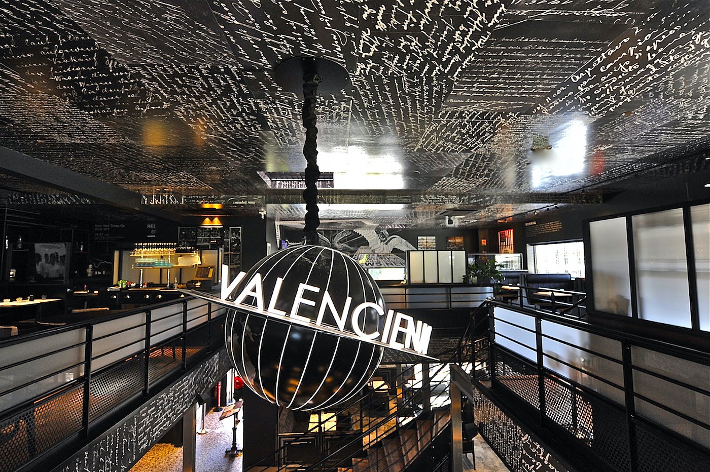 Vue en hauteur d'un restaurant moderne dont le plafond noir est couvert d'écriture blanche manuscrite, avec une grande enseigne en forme de globe suspendue au centre.
